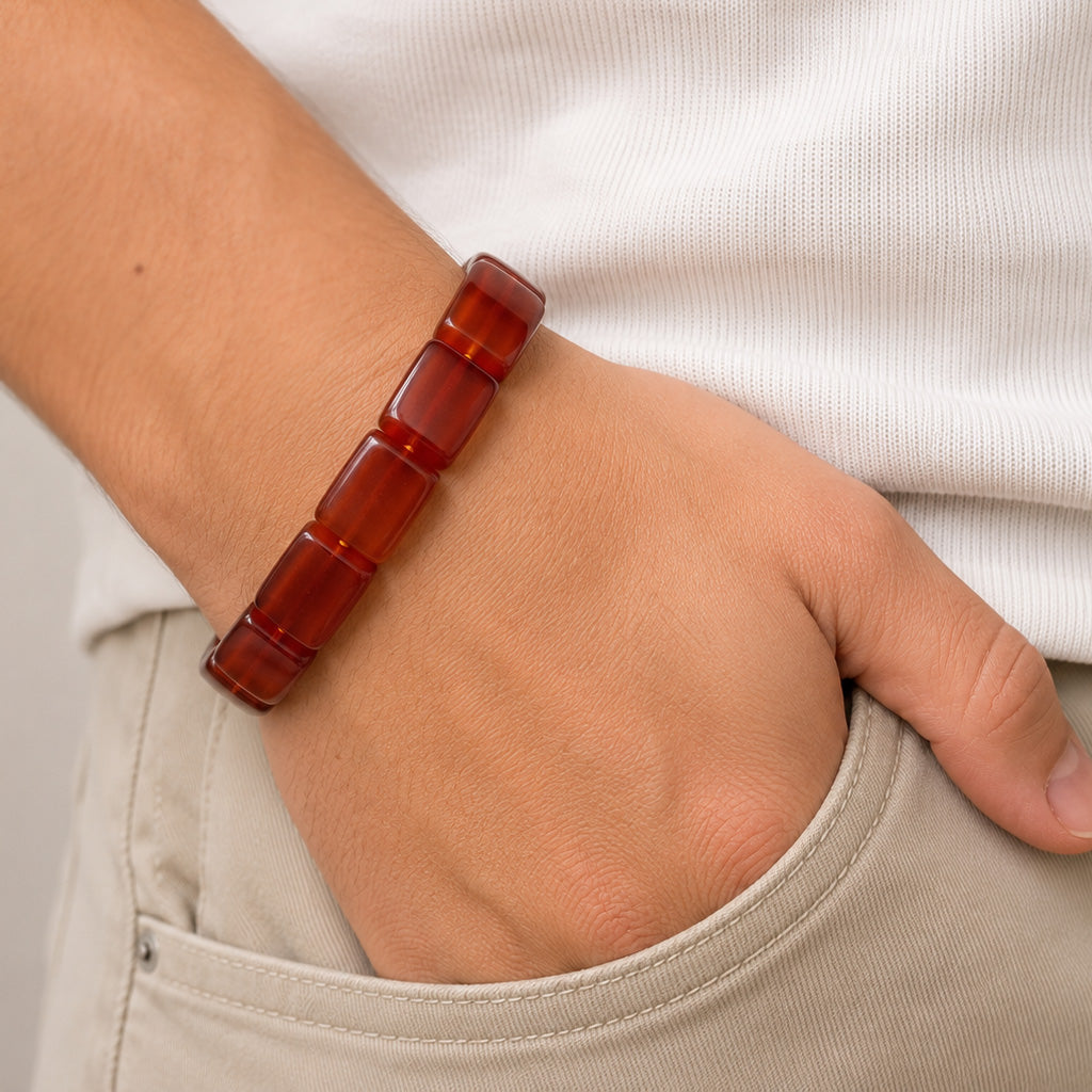 A translucent amber-red segmented beaded bracelet worn on a person's wrist, shown with a white ribbed shirt and beige pants.