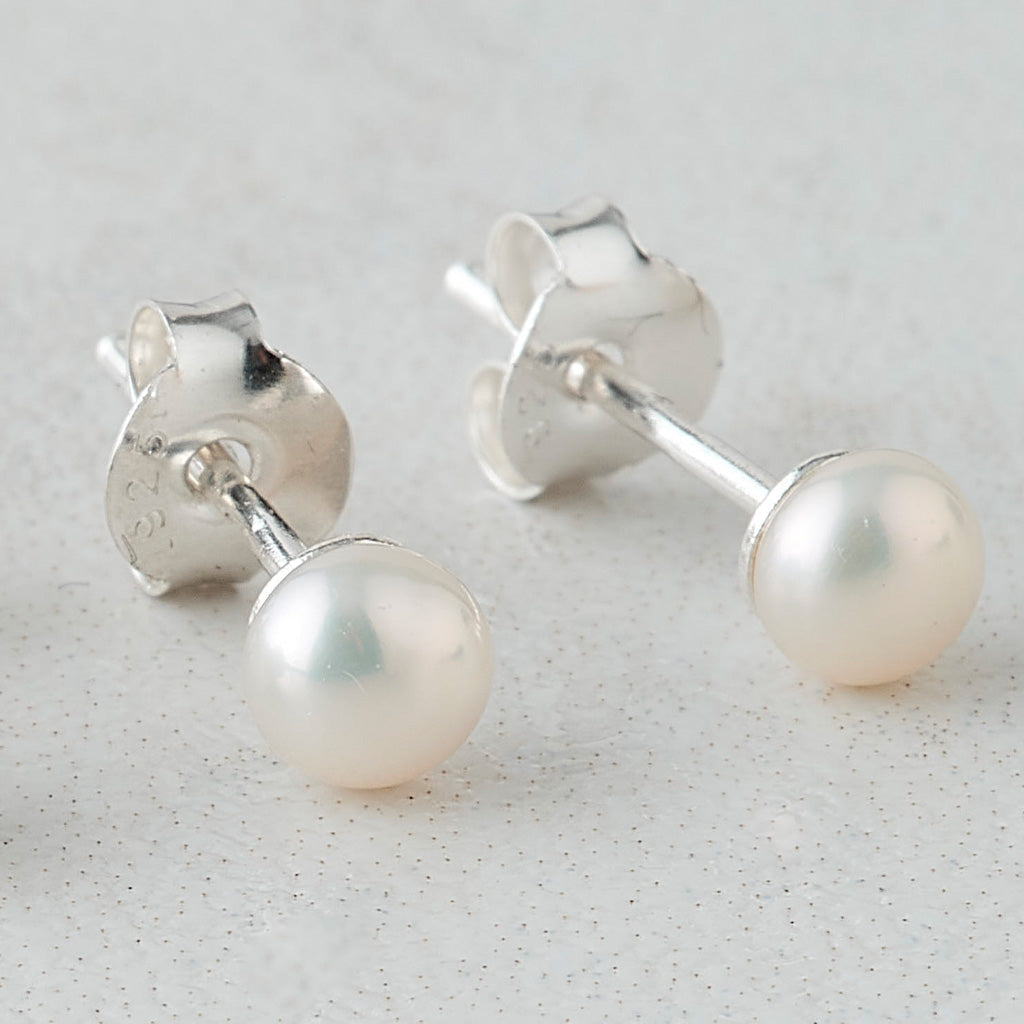 A pair of silver stud earrings with round white freshwater pearls, shown from the back on a light gray textured background.