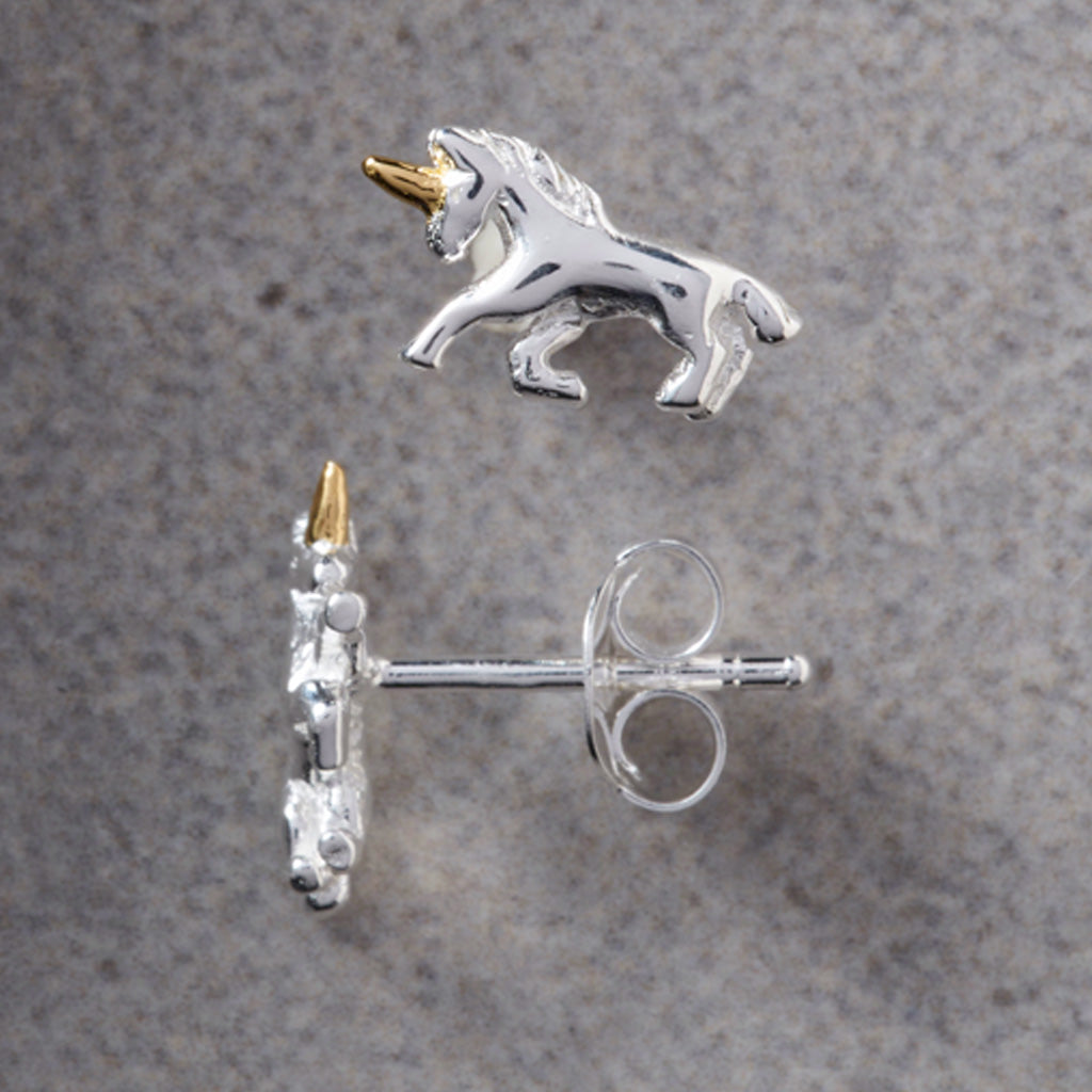 A pair of sterling silver unicorn stud earrings with gold accents, showing both the front-facing unicorn profile and the side profile with post and butterfly backing, on a textured gray background.