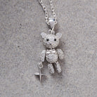 A silver teddy bear pendant necklace encrusted with clear crystals, featuring a small dangling star charm, displayed on a textured gray background.