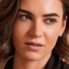 Close-up portrait of a woman wearing a small round stud earring with a silver-toned metal setting and clear gemstones, shown against her ear.