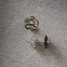 A pair of flower-shaped stud earrings with iridescent multicolor petals and silver posts, shown on a textured gray background.