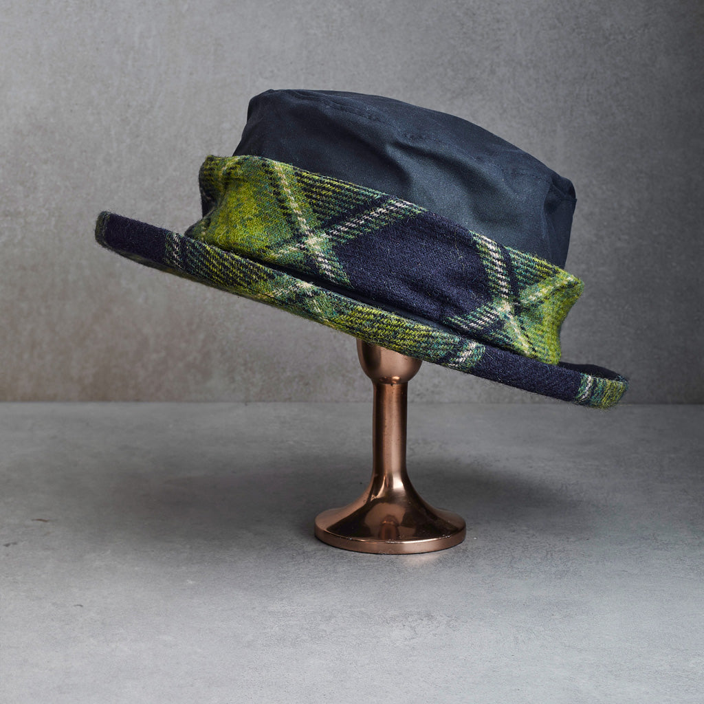  dark navy blue felt hats with green and yellow plaid wool bands, displayed on a metallic stand against a gray background.