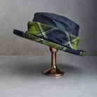  dark navy blue felt hats with green and yellow plaid wool bands, displayed on a metallic stand against a gray background.